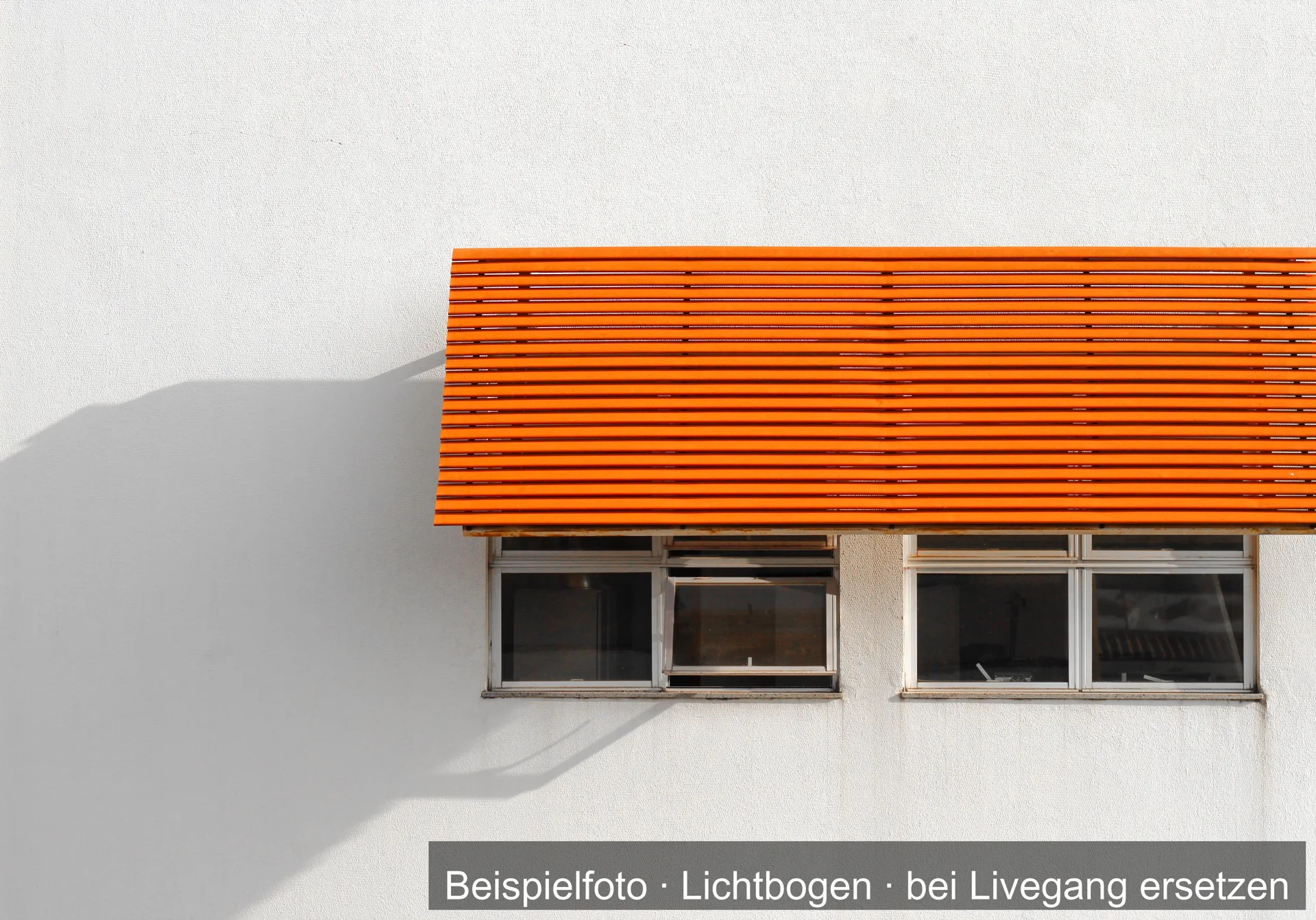 Orangefarbene Überdachung aus waagerechten Lamellen über zwei Fenstern an einer weißen Hauswand, daneben ihr Schatten.