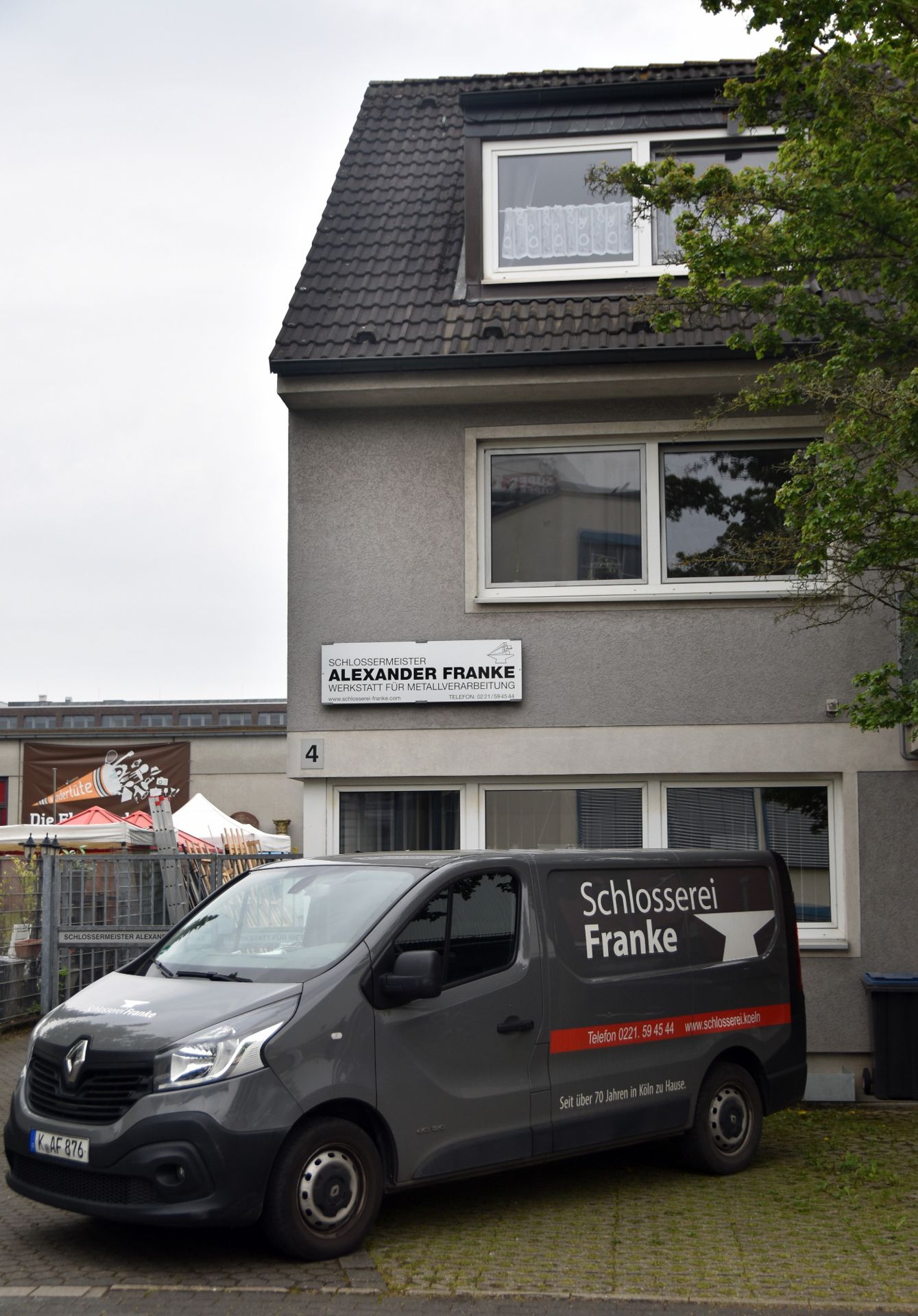 Büro- und Wohnhaus der Schlosserei an der Claudius-Dornier-Straße mit dem Schild Schlossermeister Alexander Franke, Werkstatt für Metallverarbeitung, davor der beschriftete Firmenwagen.