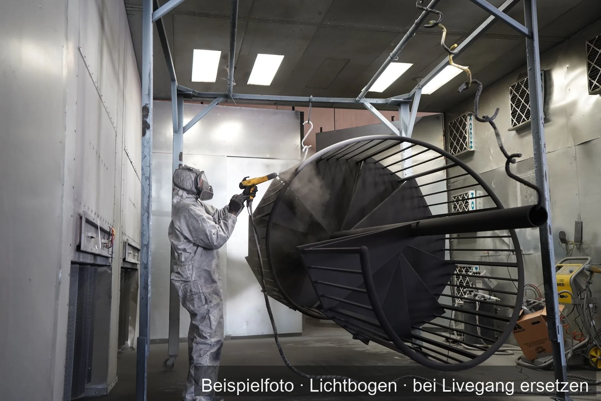 Ein Arbeiter im Schutzanzug beschichtet in einer Kabine ein großes Bauteil aus Metall.