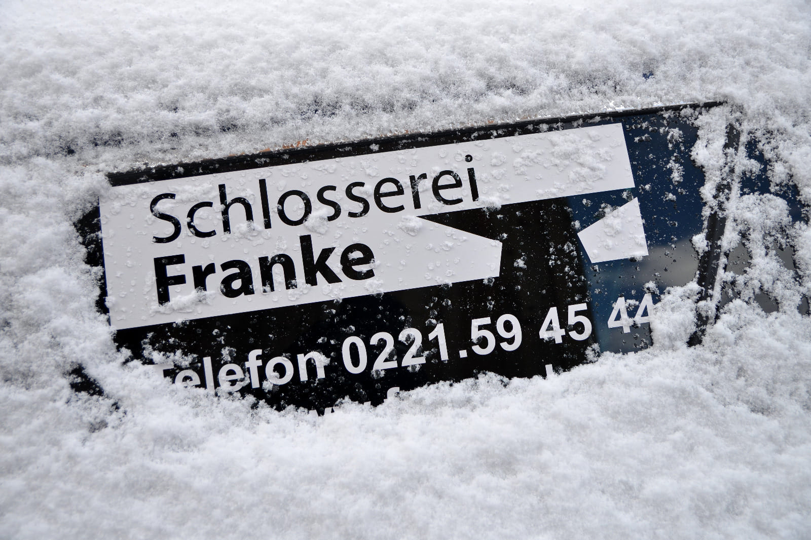 Beschriftung am Firmenwagen der Schlosserei Franke mit Telefonnummer, mit Schnee bedeckt.